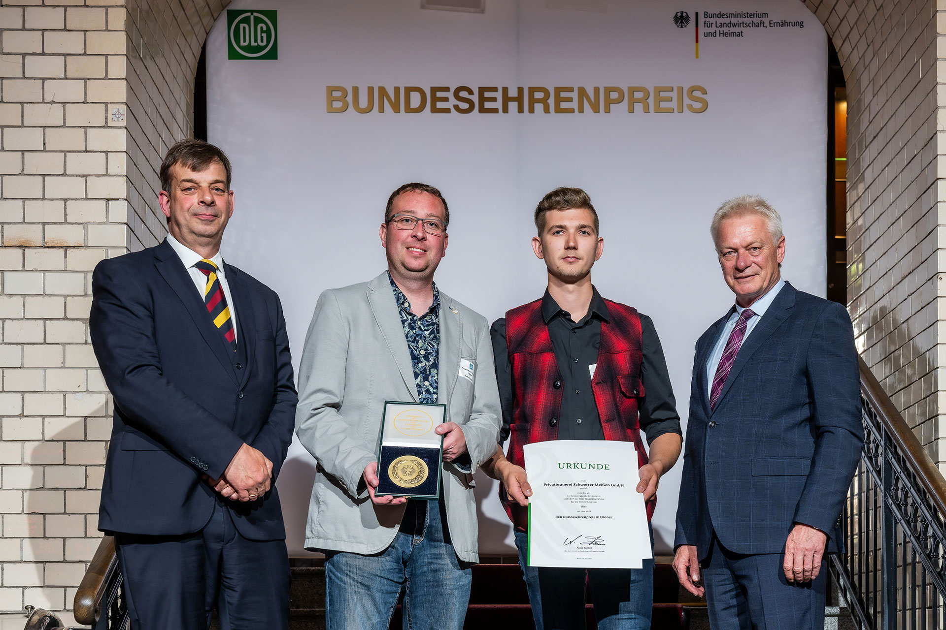 Der Bundesminister für Landwirtschaft, Ernährung und Heimat Alois Rainer (r.) überreicht mit dem DLG-Präsidenten, Hubertus Paetow (l.), die Urkunde und Medaille an Braumeister Robert Kaesler (2.v.l.) und Brauer Oliver Herzog.